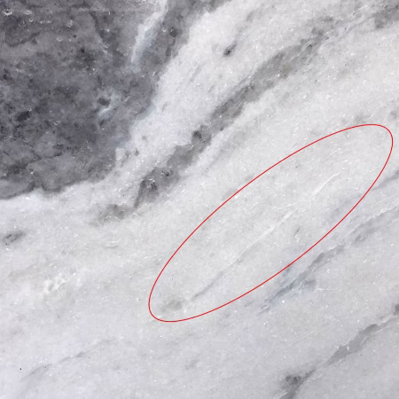 Photograph of a piece of polished veined white marble. In white-coloured marbles, it is common for NOA tremolite to be identified in features such as opaque white veins or grey-white veins (circled) that look different to the surrounding stone.