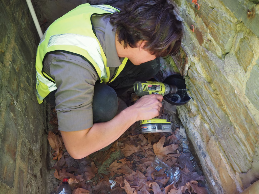 Technician in high-vis vest drilling heritage wall to obtain sample.